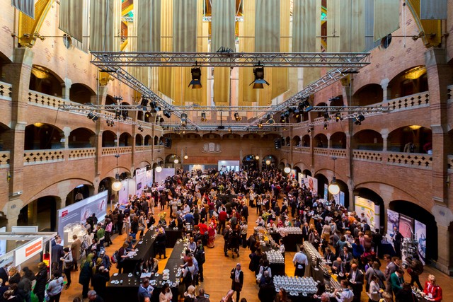 An arcaded historic hall filled with delegates and exhibition stands